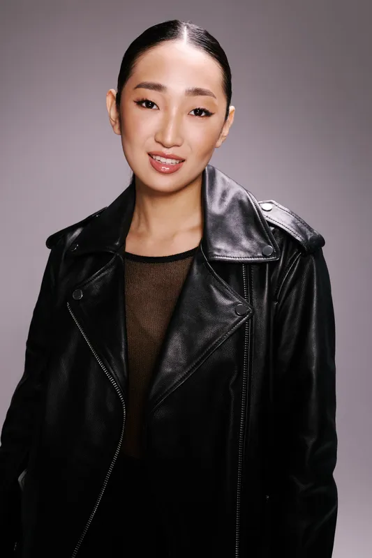 Азиатская женщина в черной кожаной куртке позирует для фото на сером фоне