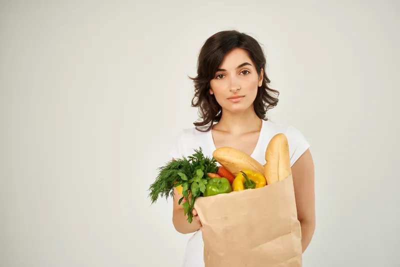 Весёлая брюнетка в белой футболке с пакетом продуктов, доставка из супермаркета