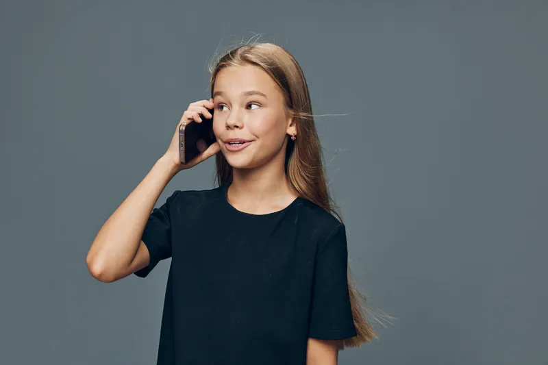 Girl with long hair talking on smartphone, smiling and looking aside on gray background. Communication, technology and youth with casual black shirt and happy expression.