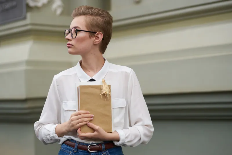 Красивая студентка с книгой в руке возле здания, обрезанный вид