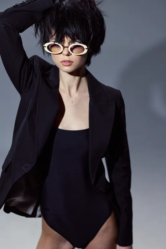 Stylish woman wearing black blazer and sunglasses posing confidently with a short hairstyle and neutral expression