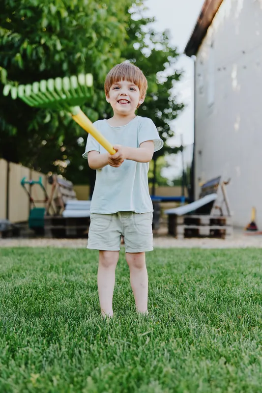 Playful boy enjoying outdoors with a colorful bat, bright sunlight illuminating a cheerful backyard setting, perfect for family fun and summer activities.