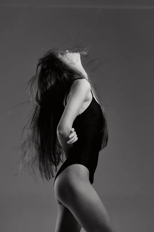 Black and white artistic portrait of a woman in a bodysuit expressing freedom and movement with long hair and dynamic pose.