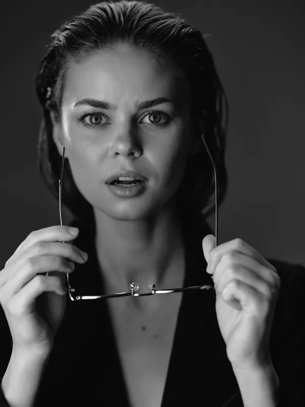 Black and white portrait of a surprised woman holding glasses with intense eyes and natural makeup