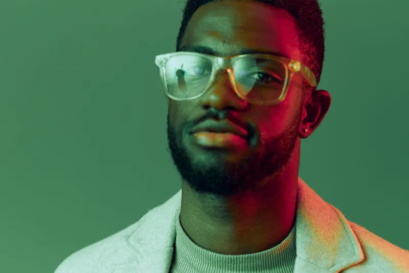 Young African man with stylish glasses in a colorful neon setting, showcasing confidence and modern fashion trends for contemporary portrait photography