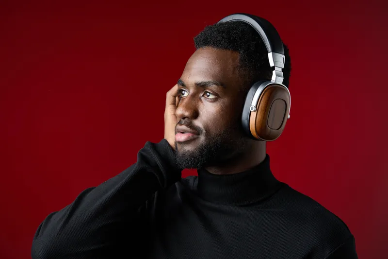 A thoughtful young Black man wearing stylish headphones against a rich red background, exuding a sense of calm and introspection while enjoying music