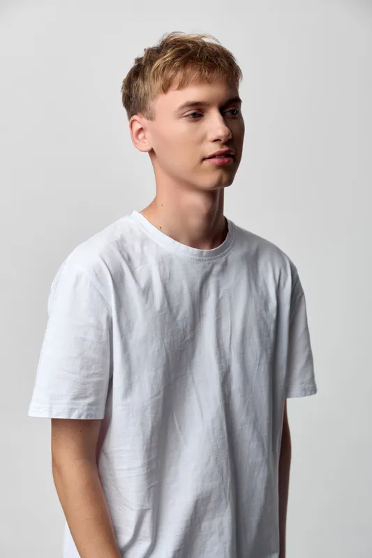 Man in a white t shirt stands in a studio with a neutral backdrop, casual posture, soft lighting, minimal fashion vibe suitable for lifestyle and stock photography