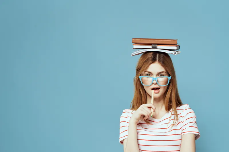 Студентка держит книги на голове на фоне синего цвета, что символизирует научное образование
