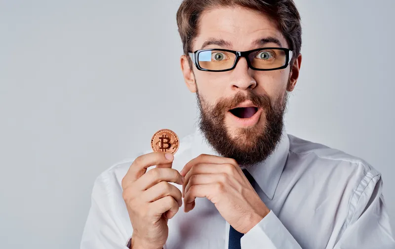 Мужчина с монетой в руке, успех, радость, криптовалюта Bitcoin, серый фон