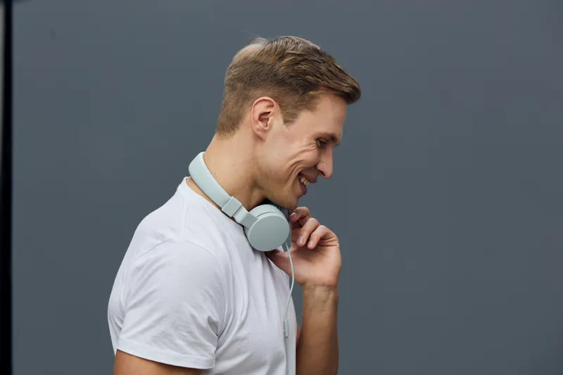 Smiling young man wearing white t-shirt with headphones around neck on plain gray background studio portrait. People lifestyle concept