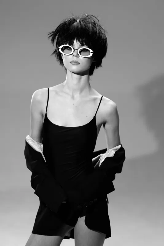 Black and white portrait of stylish woman wearing sunglasses and fashionable outfit in studio lighting.