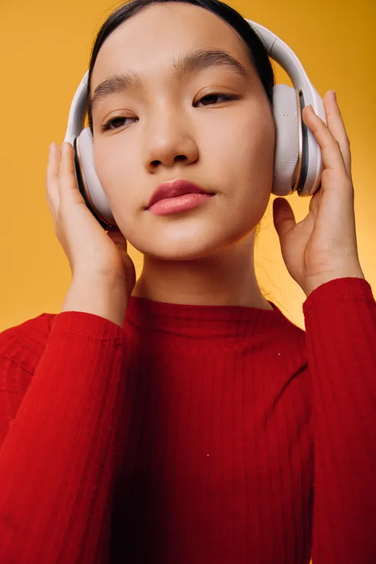 Woman with headphones listening to music or podcast wearing red sweater on orange background. Closeup portrait with eyes closed enjoying audio and relaxing with wireless headset.