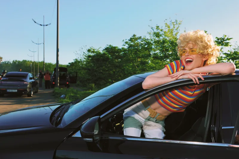 Smiling child leaning from a sleek car window in a striped shirt, capturing a retro lifestyle moment filled with joy, color, and carefree outdoor energy. Bright sunlight adds warmth to a vintage