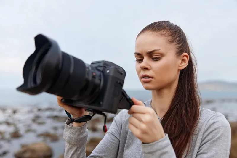 Young woman capturing nature with a camera, showcasing concentration and creativity in a serene outdoor setting surrounded by rocks and water