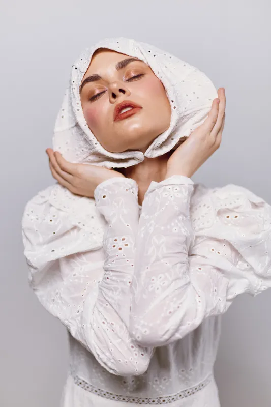 Elegant woman in white dress with headscarf expresses serenity and grace against a minimalist background, perfect for fashion and portrait photography