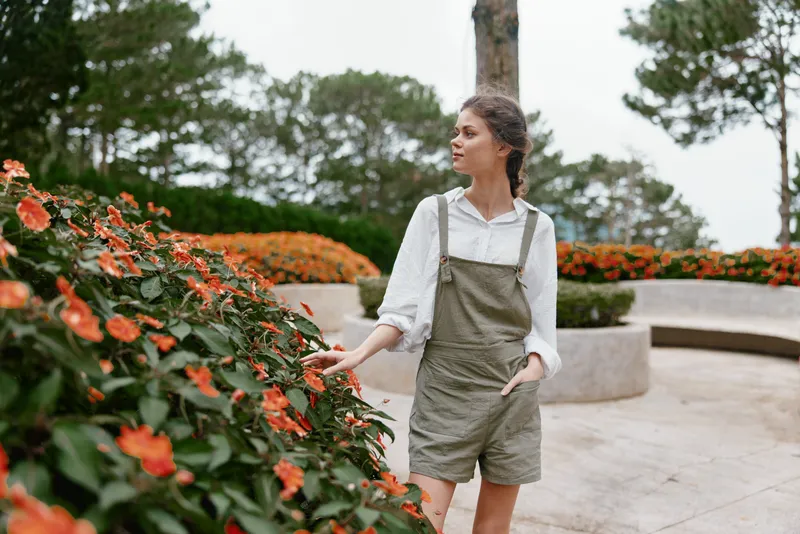 Young woman in casual overalls surrounded by blooming flowers, expressing a sense of tranquility in a vibrant garden setting