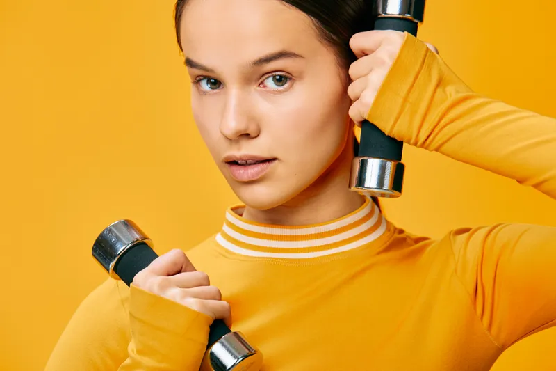 Woman fitness sport exercise training dumbbells workout athletic health strength in a vibrant orange studio, showing focus, power and determination during a workout session.