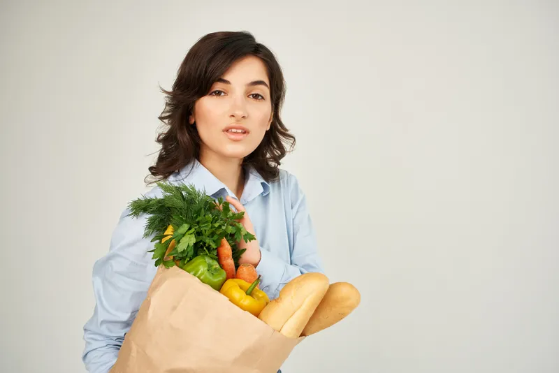 Брюнетка с пакетом продуктов из супермаркета: здоровая еда, овощи