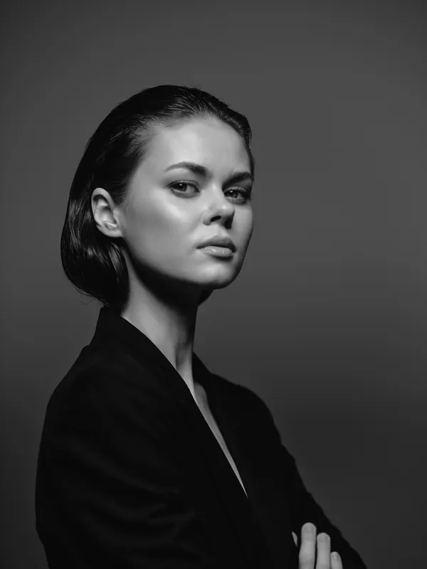 Black and white portrait of a confident woman with sleek hair and serious expression in a dark setting.