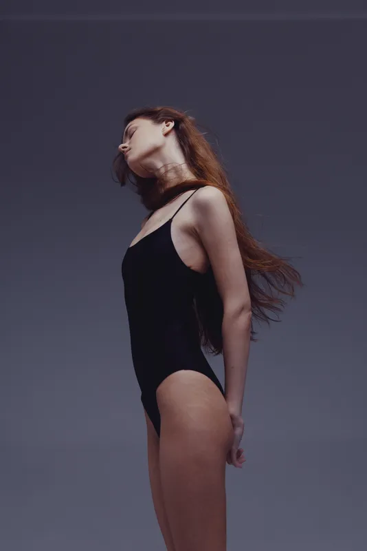 Graceful woman in black bodysuit posing with closed eyes against dark background, expressing elegance and calmness.