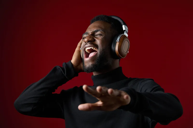 Joyful young man singing passionately while wearing headphones against a red background, capturing the essence of music and emotion in a stylish manner