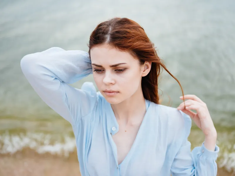 Счастливая женщина в прозрачной рубашке стоит у моря на пляже