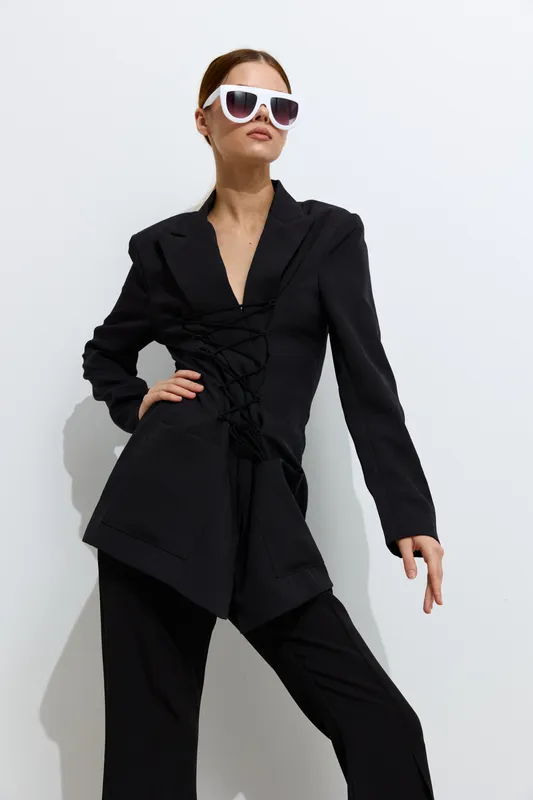 Fashion woman in stylish black outfit wearing white sunglasses poses confidently against a white background, showcasing modern beauty and chic minimalist fashion design.