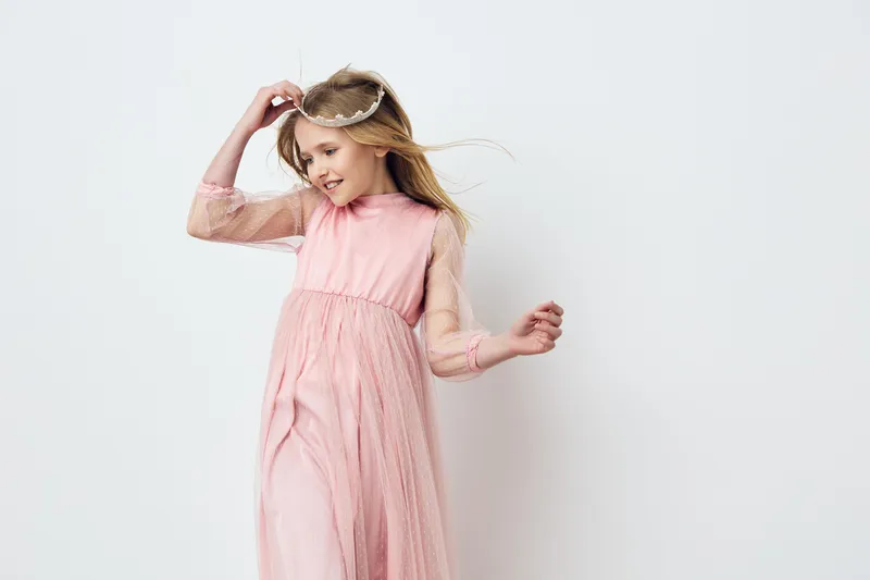Charming young girl in a light pink dress, joyfully dancing against a minimalistic background, capturing the essence of innocence and happiness, perfect for childhood concepts