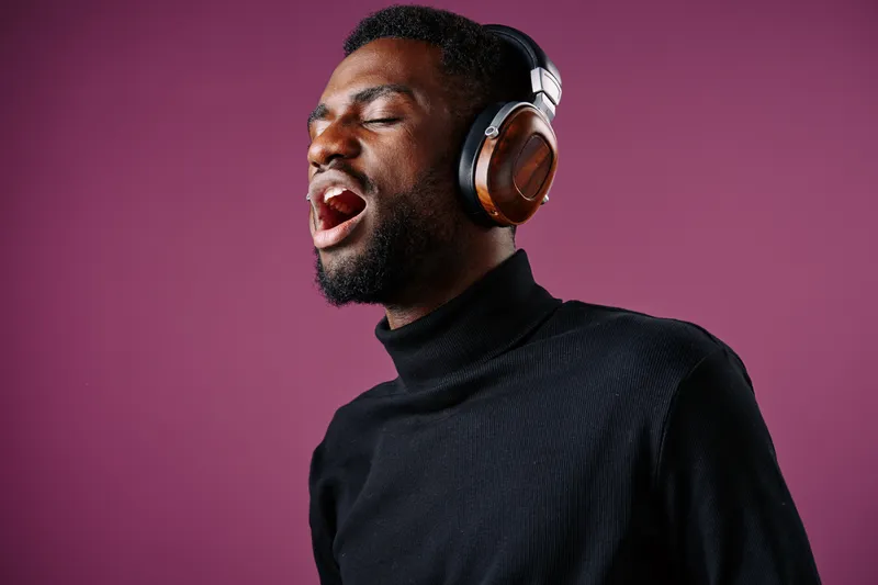 Young Black man passionately singing while wearing stylish headphones against a vibrant purple background, conveying emotions of joy and creativity