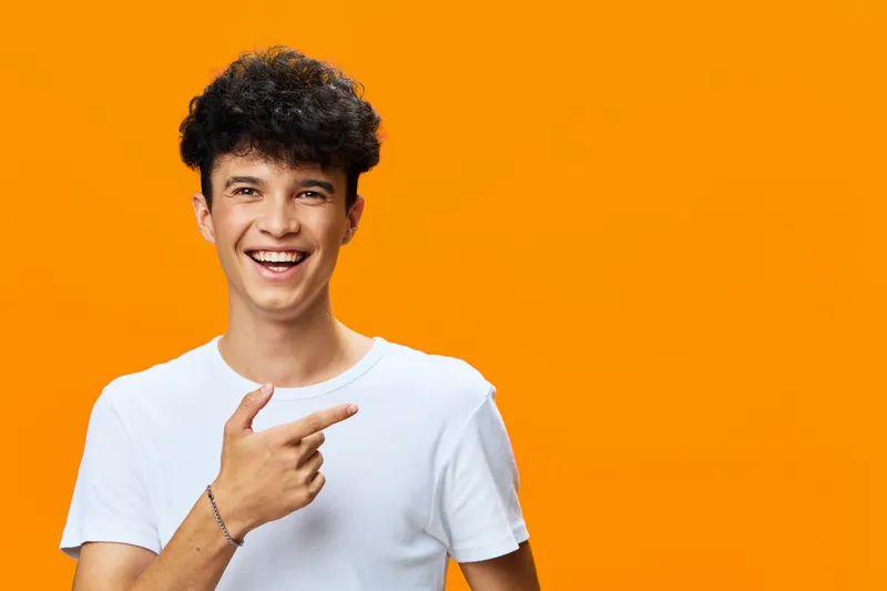 smiling man in white t-shirt pointing finger with cheerful expression against vibrant orange background, casual style, young adult, positive mood