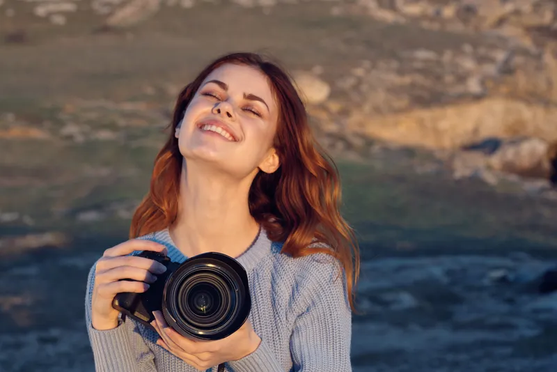 Жизнерадостная женщина-фотограф с камерой на фоне природы, пейзаж, образ жизни