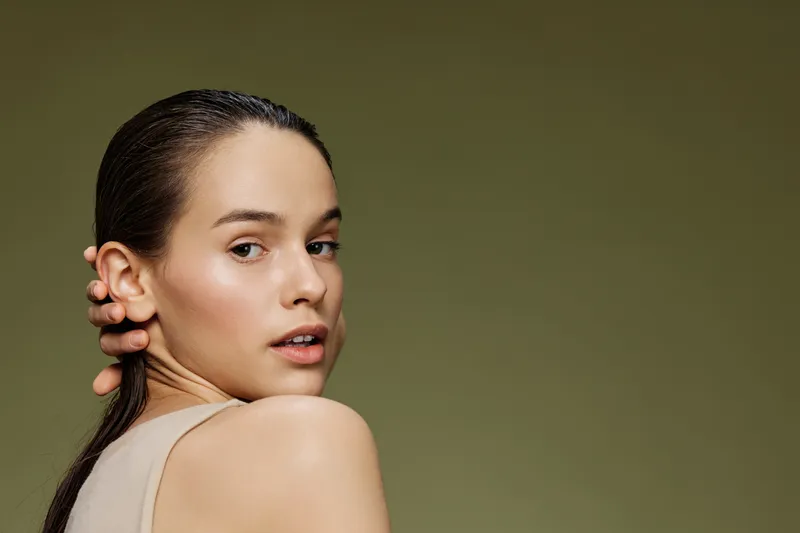 Close up portrait of a young woman with natural makeup and wet hair, set against a soft green background, portraying beauty and confidence