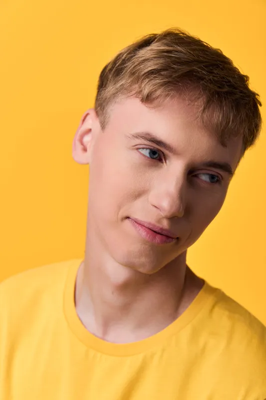 Man in a yellow shirt with a gentle smile against a bright yellow background, close up shot, casual studio lighting, clean skin and modern style, inviting mood.