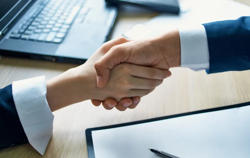 Сотрудники пожимают друг другу руки на работе в офисе, рядом лежат документы о соглашении и ноутбук