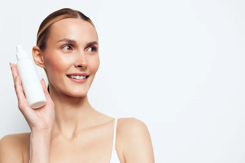 Smiling woman holds skincare face serum bottle applying cosmetic cream for hygiene skin care routine beauty closeup portrait isolated on white studio background