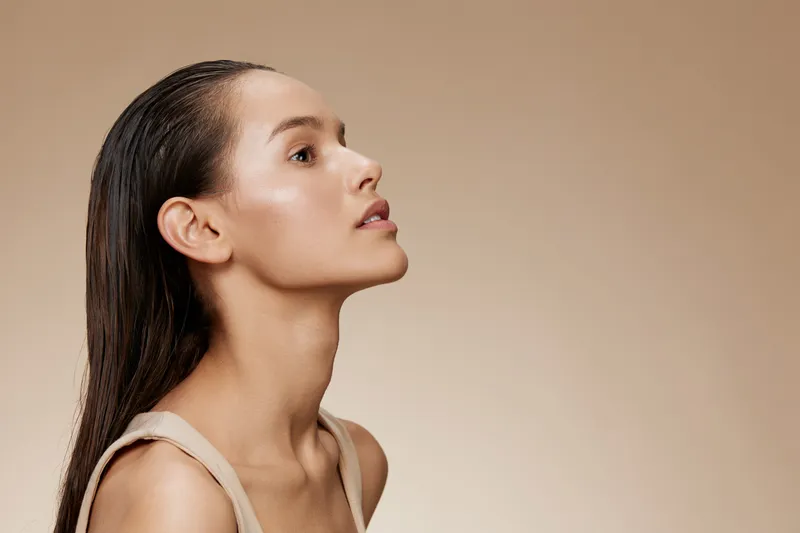 Profile portrait of a young woman with sleek hair, showcasing healthy skin and a serene expression against a warm beige background