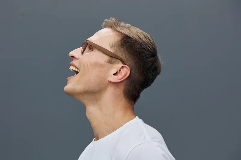 Smiling man with glasses and short hair looking upward in profile portrait on plain neutral background in studio. Happy, cheerful expression, young adult, casual white t-shirt, lifestyle concept, posi