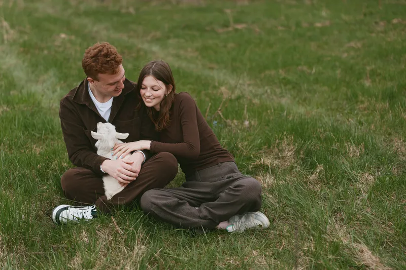 A couple sits on green grass outdoors cuddling a small white rabbit, sharing affection and happiness, a relaxed lifestyle portrait with warm, intimate mood.