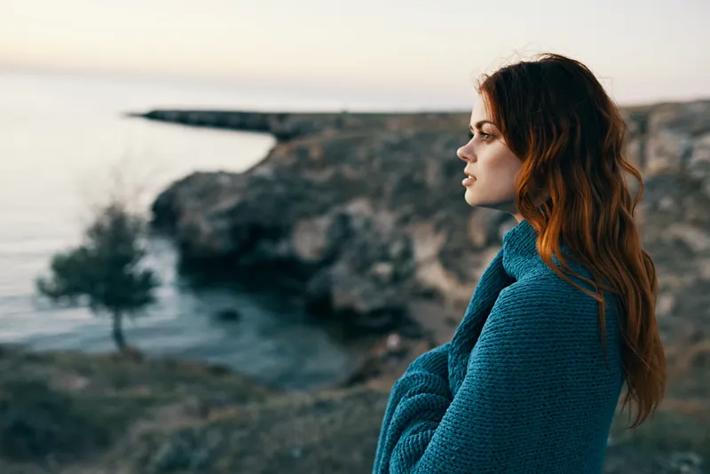 Красивая женщина в горах с пледом на плечах возле моря, модель у дерева