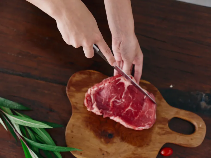 Женщина с ножом в руке нарезает свежее стейковое мясо для запекания на кухне