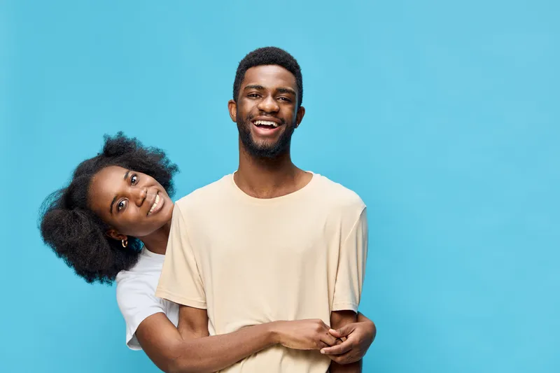 Happy African American couple embracing against a bright blue background, showcasing joy and love in casual outfits, ideal for relationship themed content