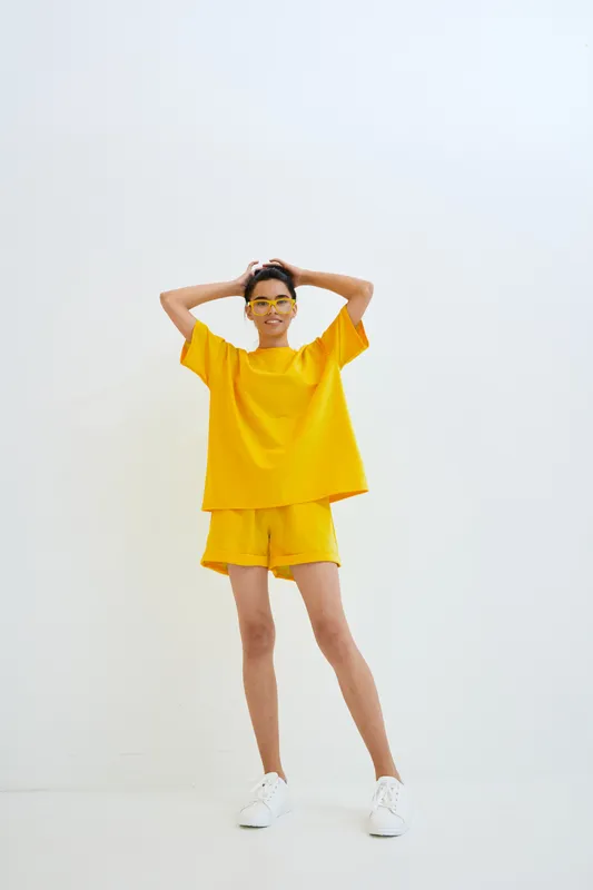 young woman wearing bright yellow casual outfit and glasses smiling joyfully standing against white background in a minimalistic setting
