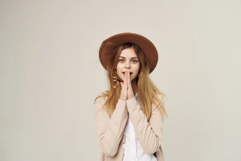 Привлекательная женщина в шляпе позирует на бежевом фоне