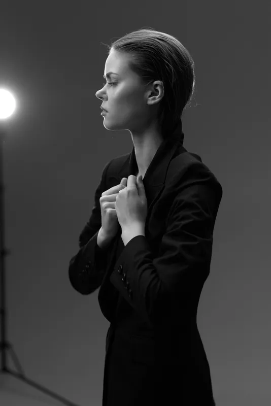 Black and white portrait of a serious woman wearing a jacket with dramatic studio lighting and a minimalist background.