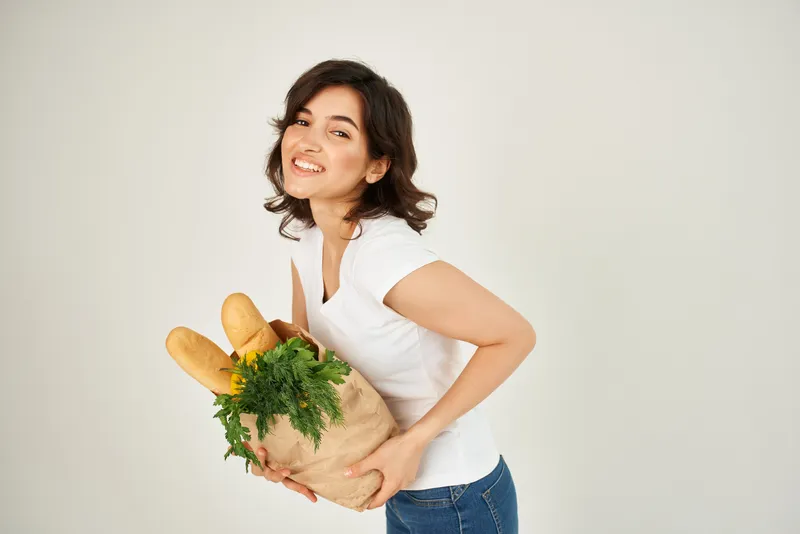 Весёлая женщина в белой футболке с пакетом овощей и продуктов
