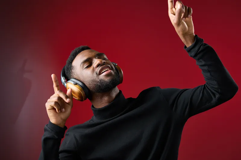 Young man enjoying music with headphones, showing joy and confidence on a red background, perfect for concepts of happiness and music enjoyment