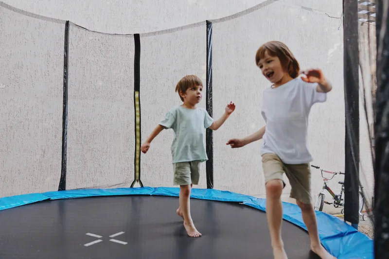 Happy children playing on a trampoline, enjoying outdoor fun with laughter and joy, testing their energy and athletic skills in a safe environment.