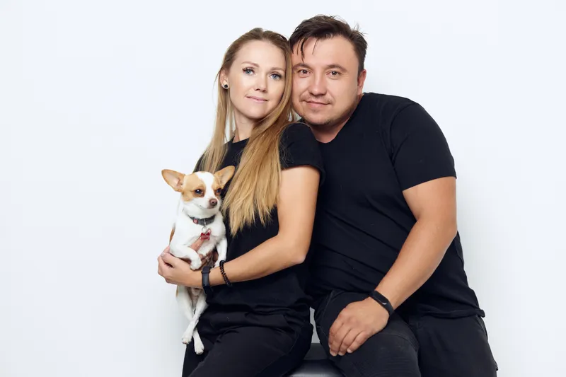 Супружеская пара обнимается на фото, рядом с ними маленькая собака в студии