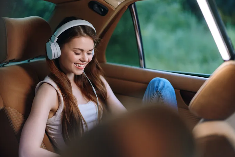Young woman listening to music with headphones in a car, enjoying her free time and relaxed atmosphere, surrounded by nature in a serene setting.