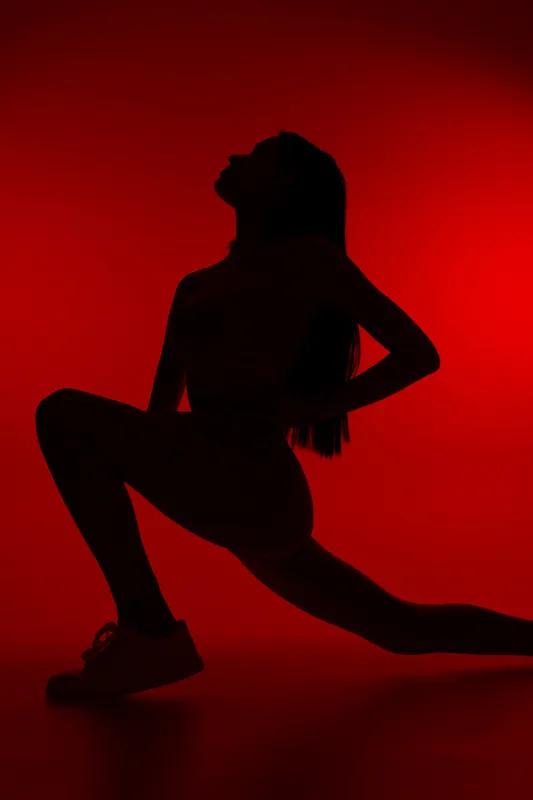 Silhouetted woman sport fitness stretching against vibrant red background, showcasing strength, flexibility, and athletic pose in dynamic low light setting.